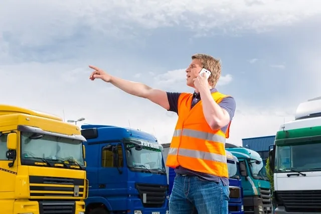 Worker in a high-visibility vest pointing in a truck parking lot.